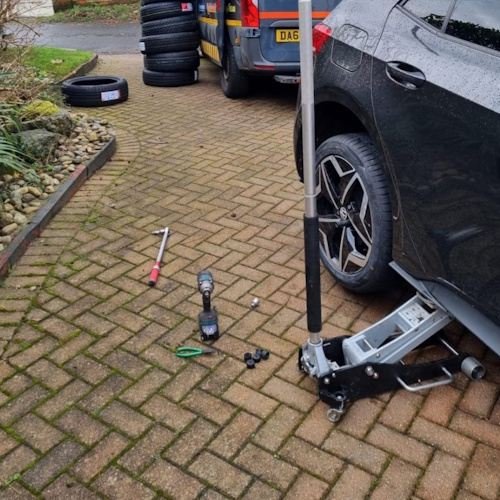 Black car tyre fitting with tools and jack in
          place